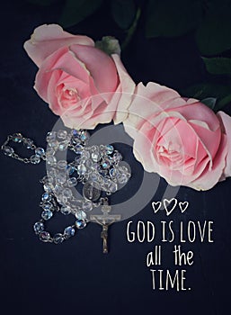 Christian inspirational quote - God is love all the time. With pink rose and Catholic rosary beads with Jesus Christ holy cross.