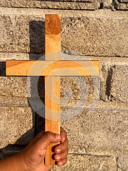 Christian kid holding a wooden cross in his hand as symbol of faith with bricks wall background. Christianity concept.