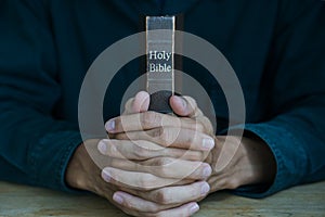 Christian man holding bible. Hands folded in prayer on a Holy Bible on wooden table