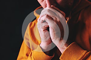 Christian man praying to God in dark room with clasped hands