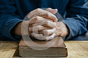 Christian man read bible. Hands folded in prayer on a Holy Bible on wooden table