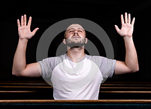 A Christian man in white shirt is sitting with his hands up and praying with humble heart in the church