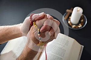 Christian praying with rosary in his hands with interlocked fingers