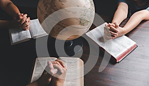 Christian small group praying together around a wooden table with bible page in homeroom. Christian group praying for globe and