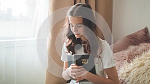 Christian teenage girl holds bible in her hands. Reading bible in a the living room. concept for faith, spirituality and religion