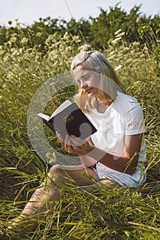 Christian teenage girl reading the Bible in the field. Faith, spirituality and religion concept