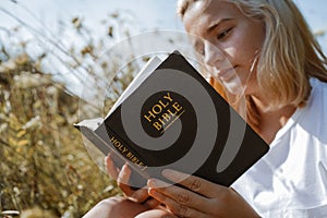 Christian teenage girl reading the Bible in the field. Faith, spirituality and religion concept