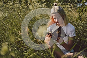 Christian teenage girl reading the Bible in the field. Faith, spirituality and religion concept