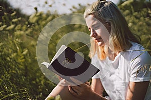 Christian teenage girl reading the Bible in the field. Faith, spirituality and religion concept