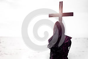 Christian woman in black holding black cross for funeral with sea and sky background. Halloween day and mourning after death of