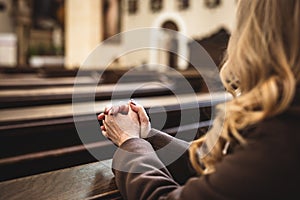 Christian woman with hands folded in prayer sitting on church pew