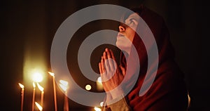 Christian Woman with Head Scarf Getting on her Knees and Praying Near the Candles in a Church. She