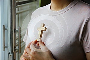 Christian woman holding a wooden cross against her chest while praying God protect
