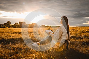 Christian woman holds bible in her hands. Reading the Holy Bible in a field during beautiful sunset. Concept for faith,