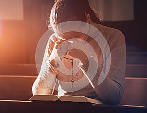 Christian woman praying in church. Hands crossed and Holy Bible on wooden desk.