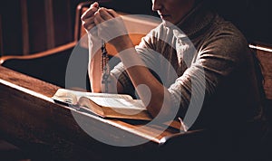 Christian woman praying in church. Hands crossed and Holy Bible on wooden desk.