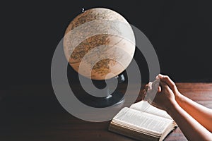 Christian woman praying for globe and people around the world on wooden table with bible. Christian hands praying together around