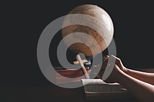 Christian woman praying for globe and people around the world on wooden table with bible. Christian hands praying together around