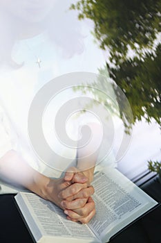 Christian woman praying with her hands folded over a bible