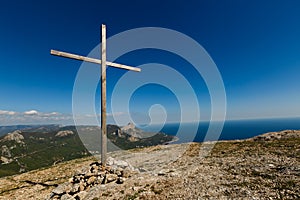 Christian wooden cross on mountain top, rocky summit, beautiful inspirational landscape with ocean, clouds and blue sky