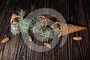 Christmas abstraction. A three waffle cones with sprigs of a Christmas tree lie on dark wood, copy space