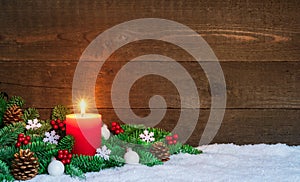 Christmas or Advent wood background with burning red candle on snow, decorated with fir branches and ornaments. Copy Space