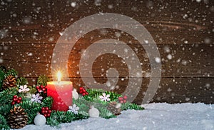 Christmas or Advent wood background with burning red candle on snow and snowflakes, decorated with fir branches and ornaments.