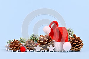 Christmas arrangement with red santa hats, pine cones, fir branches and star ornaments on blue background with copy space