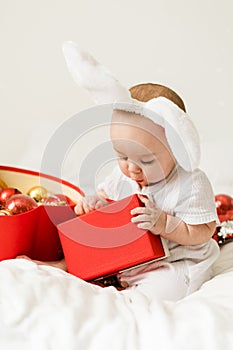 Christmas Baby Child holding christmas bauble near Present Gift Box over Holiday Lights background