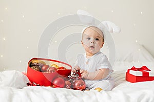 Christmas Baby Child holding christmas bauble near Present Gift Box over Holiday Lights background