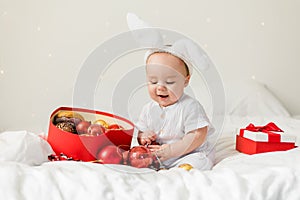 Christmas Baby Child holding christmas bauble near Present Gift Box over Holiday Lights background