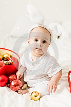 Christmas Baby Child holding christmas bauble near Present Gift Box over Holiday Lights background