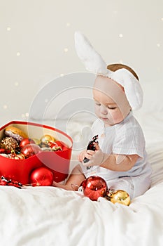 Christmas Baby Child holding christmas bauble near Present Gift Box over Holiday Lights background