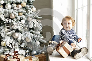 Christmas Baby , Child holding Gift Box sitting near christmas tree on the sofa at home