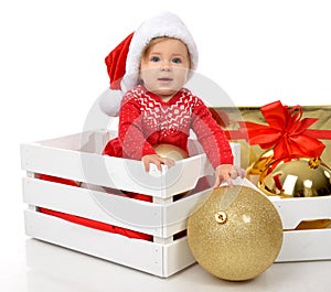 Christmas baby child in santa hat hold gold ball decoration near