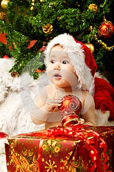 Christmas baby holding red ball near gift box