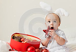 Christmas Baby in Santa Hat Child playing with baubles. Present Gift Box over Holiday Lights background and Merry