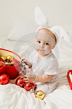 Christmas Baby in Santa Hat Child playing with baubles. Present Gift Box over Holiday Lights background and Merry