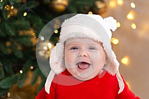 Christmas baby is smiling. A cute little girl in a red dress and white hat expresses emotions. Christmas concept with little kid,