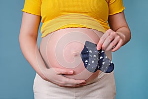 Christmas baby socks in the hands of a pregnant woman on a blue background