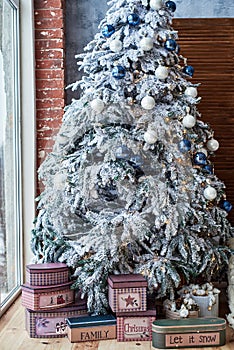 Christmas background with big Christmas fir tree with snow and white and blue decorations near window at home indoors, copy space.