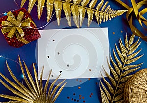 Christmas background with a blank sheet of paper, red gift boxes, golden branches of a palm tree, on a blue lilac