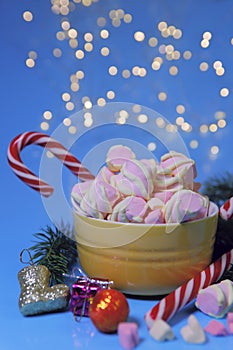 Christmas background.On a blue background with a yellow bowl with marshmallows and candy cane.