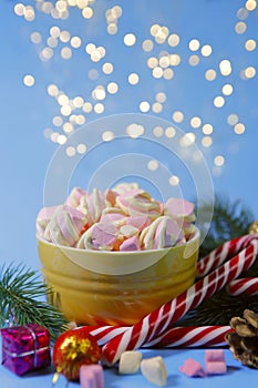 Christmas background.On a blue background with a yellow bowl with marshmallows and candy cane.