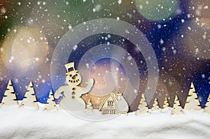 Christmas background with blue, yellow and white bokeh lights, falling snow, snowman, hut and magic forest