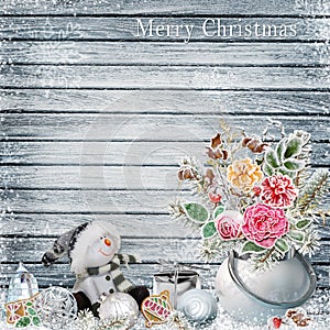 Christmas background with a bunch of flowers with frost, snowman, Christmas ornaments on a snowy wooden board