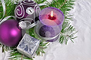 Christmas background with candle and decorations.Purple and silver Christmas balls over fir branches in the snow