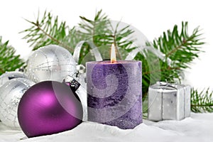 Christmas background with candle and decorations.Purple and silver Christmas balls over fir tree branches in the snow