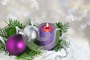 Christmas background with candle and decorations.Purple and silver Christmas balls over fir tree branches in the snow