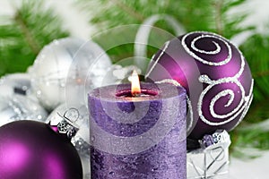 Christmas background with candle and decorations.Purple and silver Christmas balls over fir tree branches in the snow